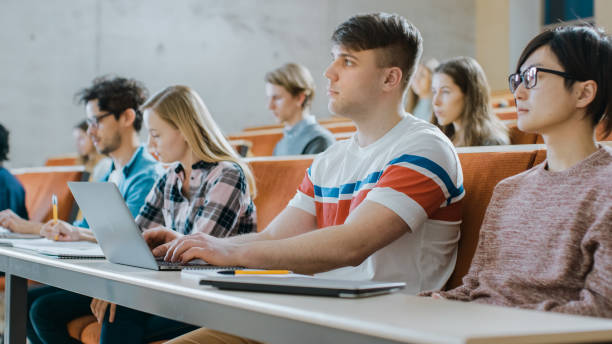 istock Handsome Caucasian Student Uses Laptop while Listening to a Lecture at the University. Multi Ethnic Group of Modern Bright Students Invested in Their Future. 962475962
