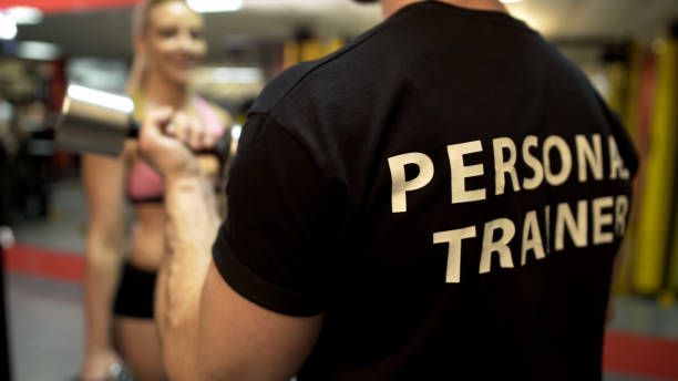 istock Personal gym trainer lifting dumbbell, showing to woman exercise technique 962476416