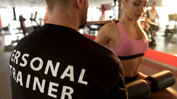 istock Fit female doing rear lat pull-down under supervision of her personal trainer 962476628