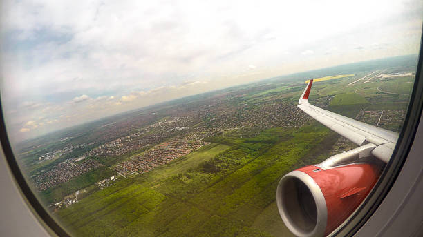 POV of flight passenger looking through window at ground, sky and aircraft wing