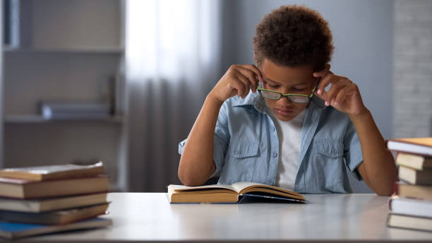 istock Concentrated school pupil in eyeglasses reading literature in library, nerd boy 962478062