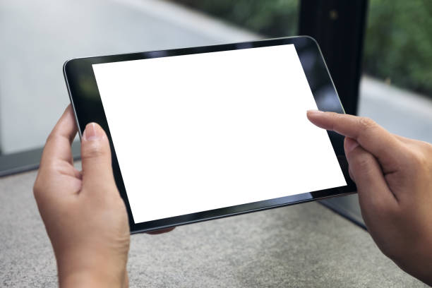 istock Mockup image of hands holding and touching a black tablet pc with blank white desktop screen on table 962486528
