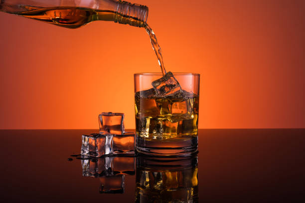 istock Whisky pouring into glass with ice drink on dark orange background 962486622