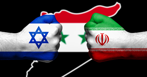 Flags of Israel and Iran painted on two clenched fists facing each other with map of Syriain the background/Israel - Iran conflict concept