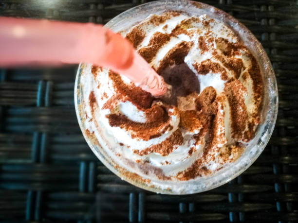 Close up overhead view depicting a creamy chocolate frappuccino drink with pink drinking straw. The frappe is dusted with cocoa powder. Room for copy space.