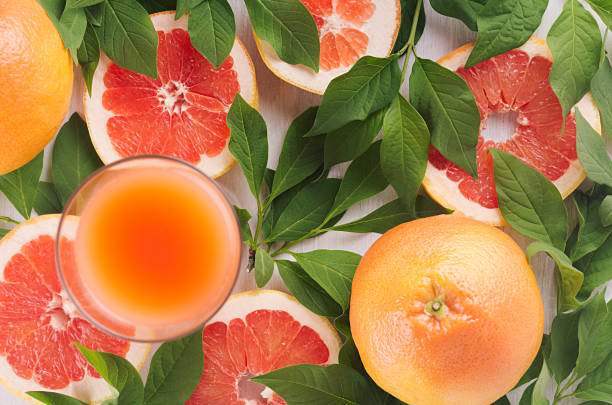 Colorful fruit pink juice with grapefruits and green leaves as fresh healthy summer background. Top view, closeup.