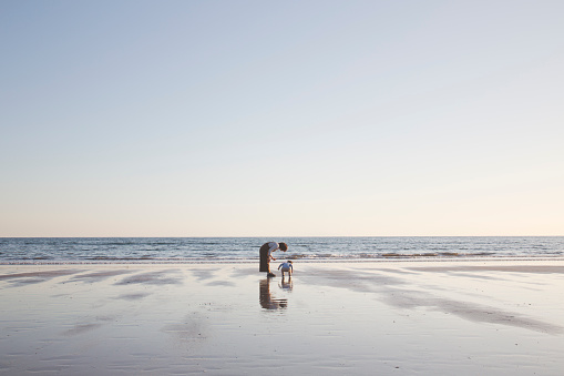 Asian mother and son looking for sea shells at sunset.