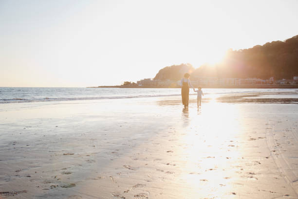 Asian mother and son holding each other's hands and walking on the beach together at sunset.
