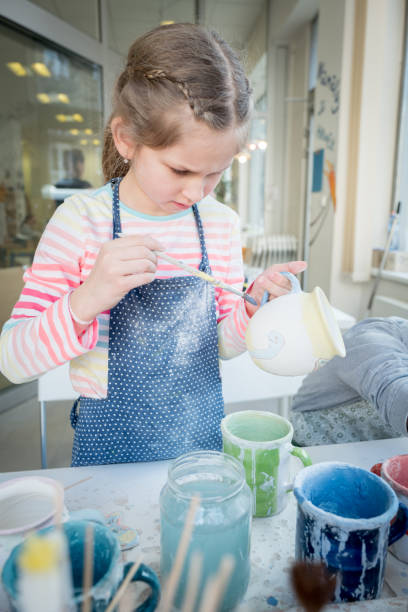 istock Skillful girl painting a clay cup at school 962511892