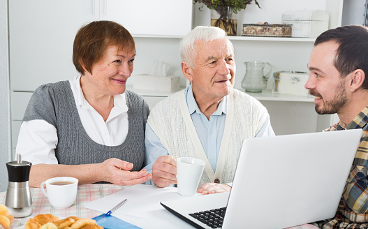 Smiling grandparents and grandson look interesting news on Internet on laptop at home