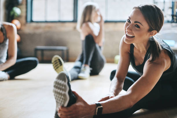 Having a laugh while limbering up Shot of mature women stretching with a young female instructor during a training class at the gym gym stock pictures, royalty-free photos & images