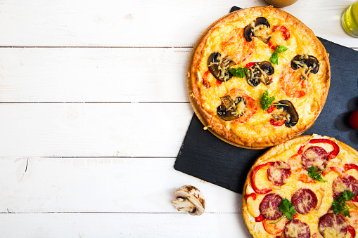 Pizza Capricciosa on a rustic cutting board, \nserved on a kitchen or restaurant table, with fresh vegetables, herbs and spices, representing a wellbeing and indulgence in food, city life and modern culture lifestyle