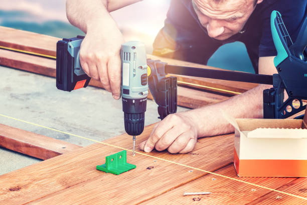 istock Construction worker screwing down wood deck with battery power screw gun or drill. 962564076