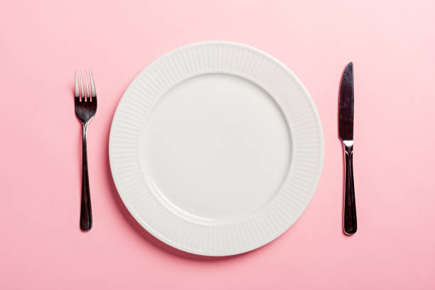 Concept To Illustrate Diet an Empty Plate An  idea to illustrate diet. A studio shot of  a dinner plate with a knife and fork. Colour, overhead view with a pink background for lots of copy space. big plate of food stock pictures, royalty-free photos & images