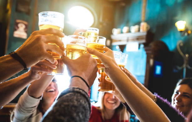 groep gelukkige vrienden drinken en roosteren biertje in brouwerij bar restaurant - concept van de vriendschap met jonge mensen samen plezier op coole vintage pub - focus op middelste pint glas - hoge iso-image - feest stockfoto's en -beelden