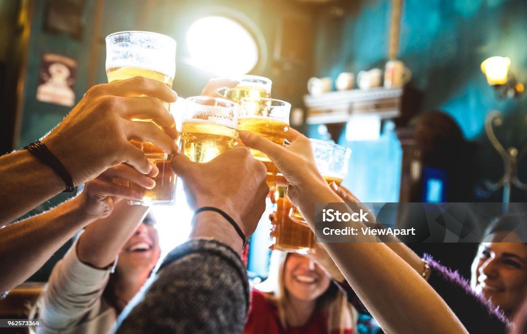 Grupo de amigos felizes, bebendo e brindando cerveja na cervejaria bar restaurante - conceito de amizade com os jovens se divertindo juntos no pub vintage cool - foco no copo médio - alto iso imagem - Foto de stock de Cerveja royalty-free