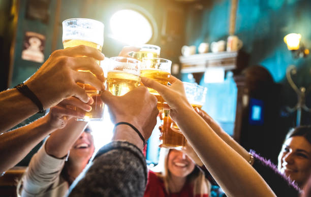 group of happy friends drinking and toasting beer at brewery bar restaurant - friendship concept with young people having fun together at cool vintage pub - focus on middle pint glass - high iso image - beer imagens e fotografias de stock