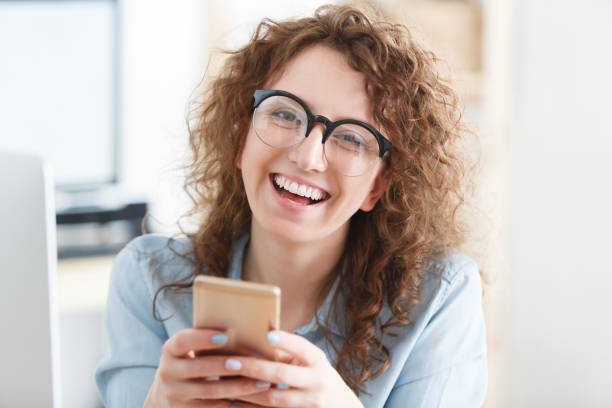 istock Pretty smiling glad woman dressed casually looking and smiling at the camera during working day. Reading information online on smart phone. People, communication and technology concept. 962580016