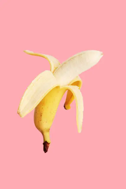 Photo of Half peeled banana on a pink background.