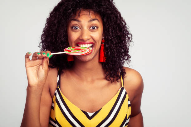Woman making a face testing, biting large colorful swirl wheel sweet candy.