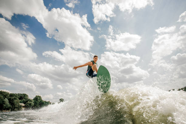 istock Young man having fun wakesurfing on the board down the river against the sky 962591910