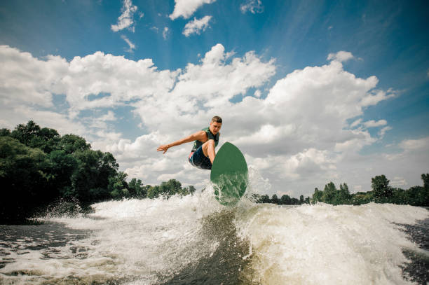 istock Active man wakesurfing on the board down the river against the cloudy sky and trees 962592142