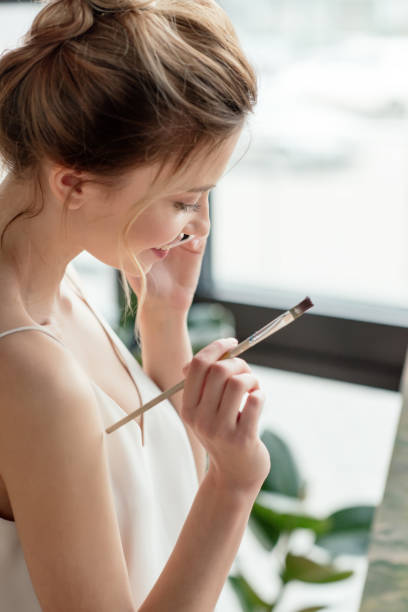 istock beautiful smiling young painter holding brush and talking by smartphone in art studio 962596206
