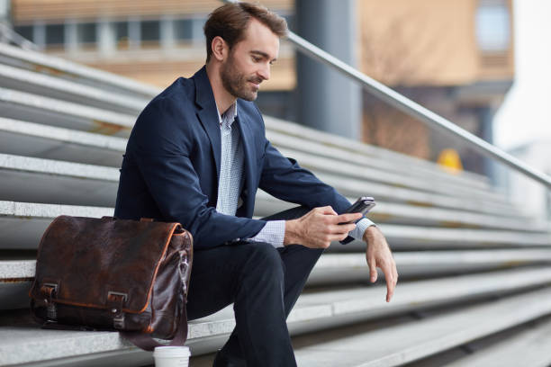 istock Businessman checking his mobile phone sitting on steps outdoor 962599490