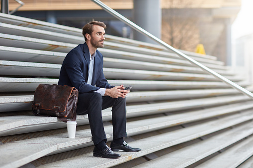 Businessman resting on steps while commuting with take away coffee.