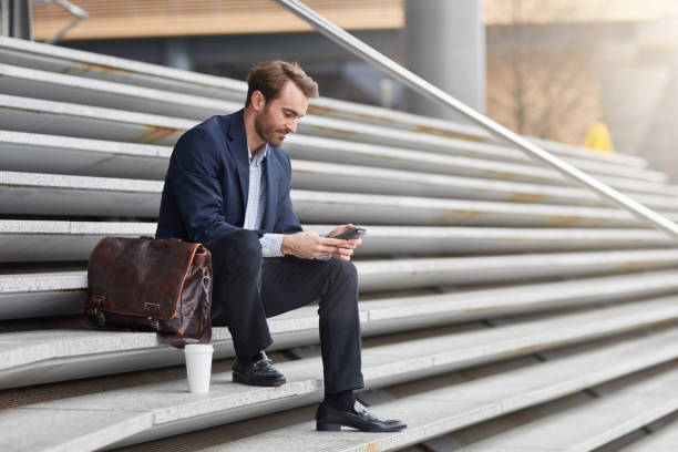 istock Businessman texting on his mobile phone sitting on steps outdoor 962599600