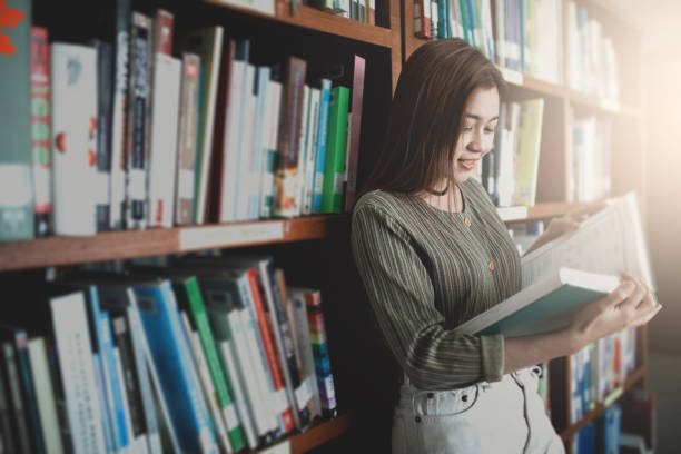 istock Young women reading book and stand front bookshelf in the library. 962604792