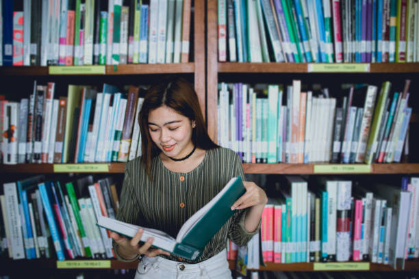 istock Young women reading book and stand front bookshelf in the library. 962604868