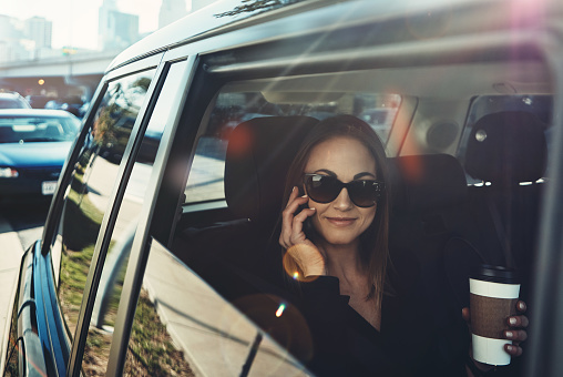 Shot of a young businesswoman using a mobile phone while traveling in a car