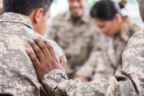 Soldiers pray during therapy session Unrecognizable soldier places his hand on fellow soldier while praying for him during a support group meeting. veteran stock pictures, royalty-free photos & images