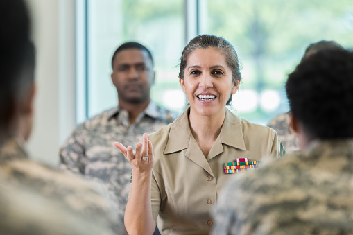 Mature Hispanic female military officer gestures while asking a question during a seminar.