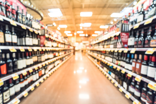 Blurred image of wine shelves with price tags on display at store in Humble, Texas, US. Defocused rows of Wine Liquor bottles on the supermarket shelf. Alcoholic beverage abstract background.
