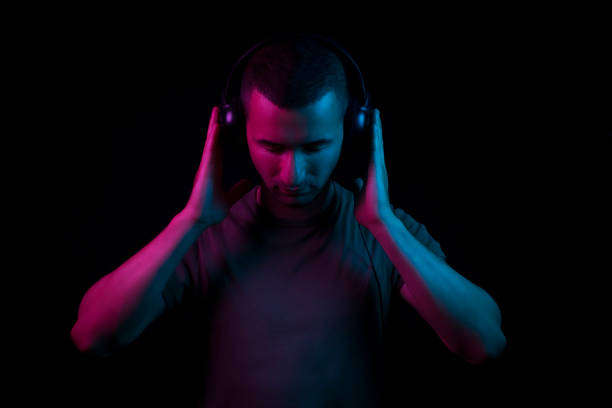 A dj holding his head set on black background under magenta and blue gel lighting