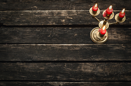 Old candlestick with four burning candles on an empty wooden table background with copy space.