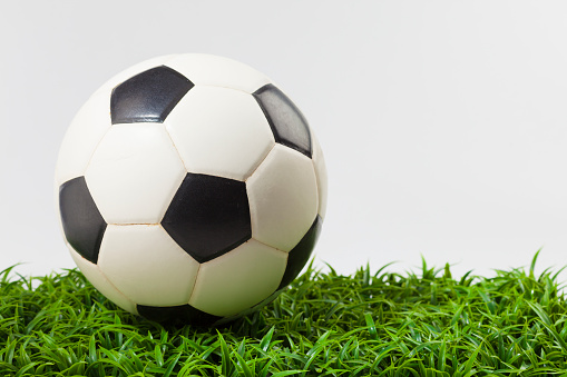 Classic soccer ball on artificial grass on white background. The ball is made of leather and has a white hexagons - black pentagons pattern. No people. Studio photography. Front view. Close-up. Horizontal orientation with copy space. Classic design.
