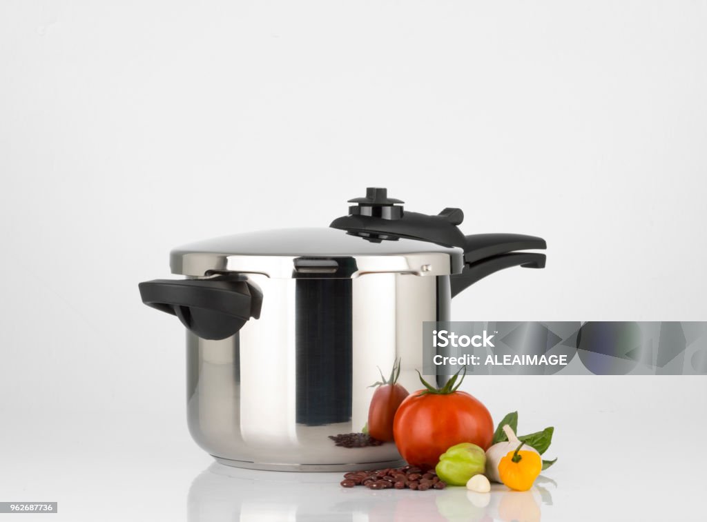 Pressure cooker Pressure cooker and vegetables on white background. The pressure cooker looks new and shining and is made of steel. There are some vegetables aside: tomato, sweet peppers, garlic, beans and basil. Studio photography with horizontal orientation and copy space. Still life photography. Pressure Cooker Stock Photo