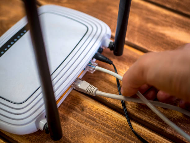 cerca mano insertar cable ethernet en el router wi-fi en mesa de madera - speed meter fotografías e imágenes de stock