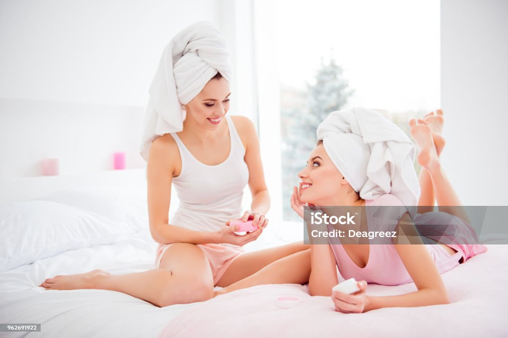 Retrato de la alegre, alegre, encantador, atractivo, bonito, limpio, claro, puras chicas lavaron cabello con toalla en la cabeza, sentado, acostado en cama, uso bálsamo cara para seco, suave suave y engrasado piel - Foto de stock de Crema hidratante libre de derechos