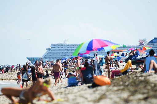 Miami - April 29, 2018: A cruise ship leaves port in the background as people crowd South Beach on a bright weekend afternoon.