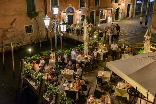 Venice, Italy - August 26, 2016: Venetian dining,see people sitting in a small restaurant oudside and enjoing the night