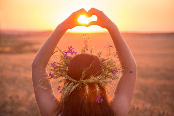 girl on wheat field making heart symbol at sunset