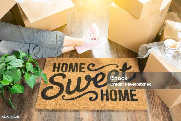 Woman Wearing Sweats Relaxing Near Home Sweet Home Welcome Mat Moving Boxes And Plant Stock Photo - Download Image Now