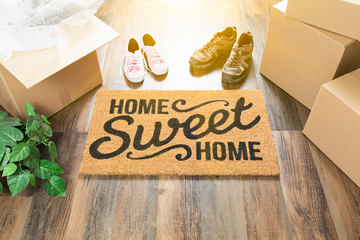 Home Sweet Home Bienvenido Mat, moviendo cajas, mujer y hombres zapatos y planta de pisos de madera. photo