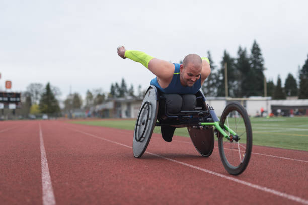 Adaptive athlete training on his racing wheelchair at a stadium track A Caucasian para athlete trains at a stadium track in his wheelchair. He is racing toward the camera and has an intense expression. athlete with disabilities photos stock pictures, royalty-free photos & images
