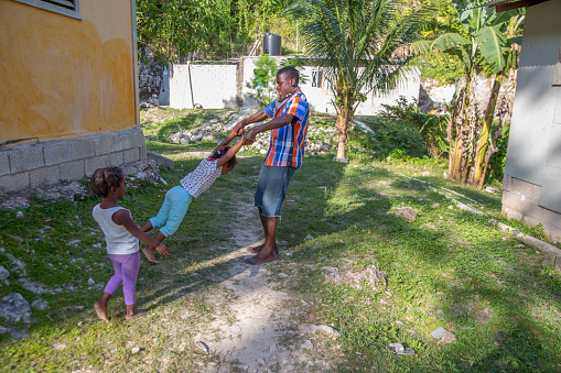 A Jamaican teenage boy is twirling his little sister in the air. Shot with Canon 5D Mark lll.
