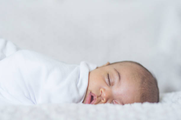 Newborn Sleeping Baby A beautiful newborn interracial baby lays swaddled and sleeping in her hospital bassinet. Her eyes are closed peacefully and she looks like she is having pleasant dreams. biracial newborn stock pictures, royalty-free photos & images